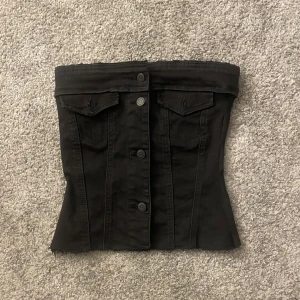 Svart tubtopp med knappar - Snygg svart tubtopp med knappar framtill och dekorativa fickor. Perfekt för en stilren look.