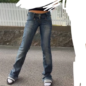 Blå, lågmidjade, bootcut jeans från Lee - Säljer ett par snygga blå jeans från Lee. Jeansen har en lätt tvättad look. De har ett litet hål något under knät. Storlek står inte i byxorna. Köpta på Plick. Innerbenslängd: 86cm, midjemått tvärs över: 36cm