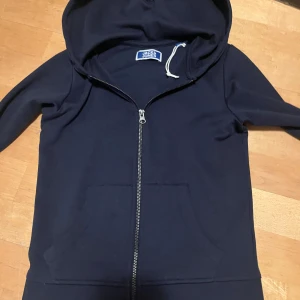 Blå huvtröja från Jack & Jones - Säljer en stilren marinblå huvtröja från Jack & Jones. Tröjan har en dragkedja framtill och praktiska fickor. Perfekt för en avslappnad stil. Tveka inte på att fråga!