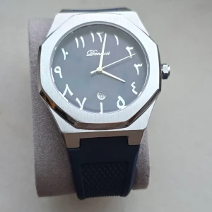 Blå klocka med silverdetaljer  - Snygg klocka med blå urtavla och arabiska siffror. Den har en robust blå rem och en silverfärgad boett. Perfekt för dig som vill ha en stilren och modern look. Klockan har även en datumvisare vid klockan sex. Datumet går att justera med kronan