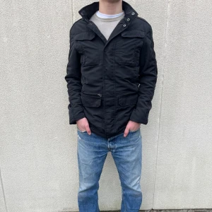 Svart jacka från Riley - Snygg svart/blå fieldjacka från Riley med dragkedja och knappar. Jackan har flera praktiska fickor och en hög krage. Perfekt för kyligare dagar. Hör av er vid frågor!👍