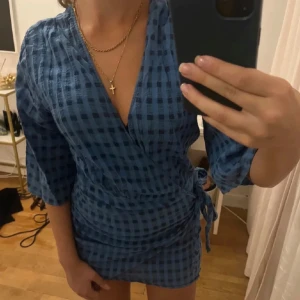 Blå Zara klänning - Säljer en snygg Zara klänning  med trekvartsärm och knytning i midjan. Perfekt för en stilren look med en touch av elegans. Klänningen har en v-ringad design som ger en feminin känsla.
