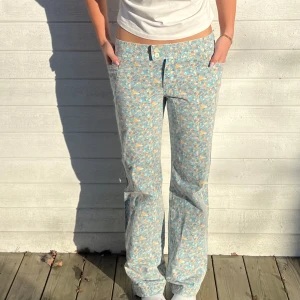 Blommiga byxor med låg midja - Snygga blommiga byxor i blått och orange med låg midja. Byxorna har en rak passform och knappar framtill. Perfekta för en avslappnad stil.