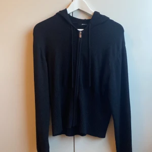 Svart kofta från Gina Tricot - En svart hoodie från Gina Tricot i storlek XL. Den har en dragkedja framtill och lång ärmad. Den har en luvan med snören för justering. Passar bra till mycket.