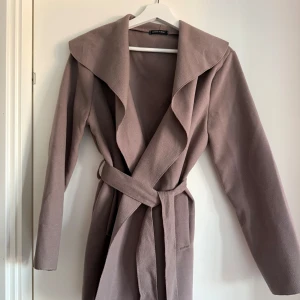 Beige kappa från Made in Italy - Elegant beige kappa med knytbälte och bred krage. Perfekt för kyligare dagar med sin långa design och stilrena look. Tillverkad i Italien, vilket ger en känsla av lyx och kvalitet.