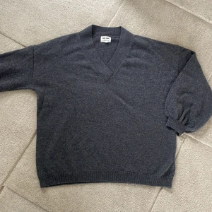 Grå kashmirtröja från Soft Goat - Säljer en elegant grå kashmirtröja från Soft Goat. Tröjan har en v-ringad design och långa ärmar med ribbade muddar. Perfekt för en stilren och bekväm look. Passar utmärkt till både vardag och mer uppklädda tillfällen.