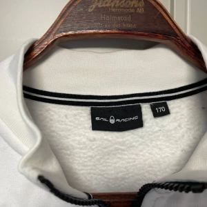 Vit tröja med dragkedja från Sail Racing - Jättefin, stilren vit tröja från Sail Racing med halv dragkedja och broderad logga på bröstet. Stl 170 knappt använd. Tvättad en gång inför försäljning. Prutat å klart!
