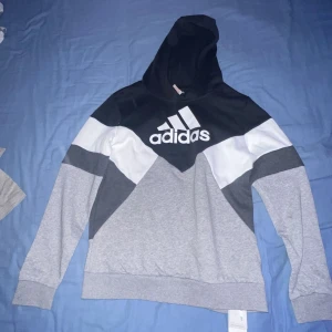 Grå och svart hoodie från Adidas - Säljer en snygg grå och svart hoodie från Adidas med vit logga på bröstet. Hör av er vid minsta fråga eller fundering. Pris kan diskuteras.
