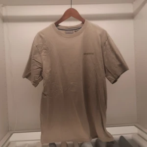 Beige t-shirt från Superdry - Säljer en stilren beige t-shirt från Superdry. Den har en klassisk rund hals och korta ärmar, perfekt för en avslappnad look. Tillverkad i ett mjukt material för extra komfort.