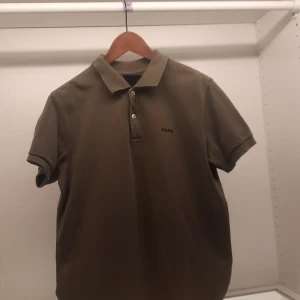 Olivgrön pikétröja från Peak Performance - Säljer en stilren olivgrön pikétröja från Peak Performance. Tröjan har korta ärmar och en klassisk krage med knappar. Perfekt för en avslappnad men ändå snygg look. Broderad logga på bröstet.