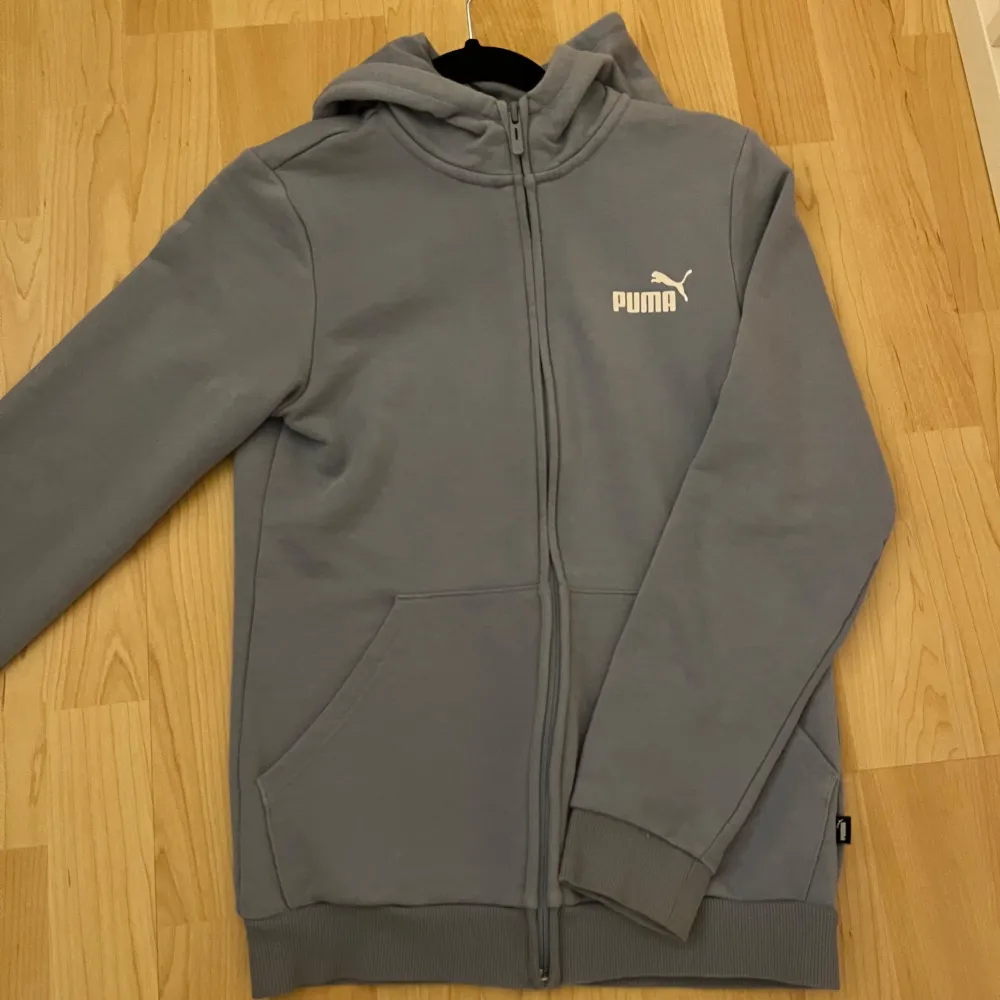 Säljer en stilren blå hoodie från Puma med dragkedja och huva. Tröjan har långa ärmar och en praktisk ficka framtill. Perfekt för en avslappnad look.. Neuletakit & Villapaidat.