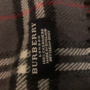 Rutig halsduk från Burberry - Snygg rutig halsduk från Burberry i grått med inslag av rött och vitt. Tillverkad i mjuk kashmir för en lyxig känsla. Perfekt för att hålla dig varm och stilren under kyliga dagar. Pris kan diskuteras! Skriv om du vill ha tydligare bild😊