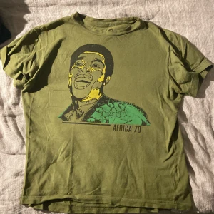 Grön t-shirt med tryck från Retrofame - Cool grön t-shirt från Retrofame med texten 'Africa '70' på framsidan. Baksidan har texten 'a tribute to the original ransom'. Perfekt för dig som gillar unika, retroinspirerade och politiska  plagg.