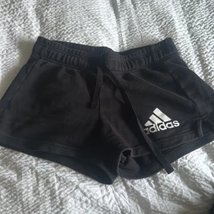 Svarta shorts från Adidas - Snygga svarta shorts från Adidas med vit logga på benet. De har en bekväm passform med snörning i midjan. Perfekta för träning eller en avslappnad dag.