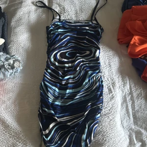 Mönstrad klänning med smala axelband - Snygg klänning med ett abstrakt mönster i blå, vit och svart. Den har smala axelband och en figurnära passform som framhäver silhuetten. Perfekt för en kväll ute eller en speciell tillställning.