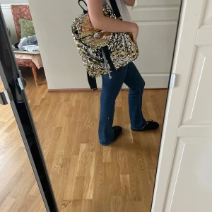 Glittrig ryggsäck med paljetter - Säljer en supercool ryggsäck täckt med glittriga paljetter i guld och silver. Perfekt för att lysa upp vilken outfit som helst. Ryggsäcken har justerbara svarta axelremmar och en praktisk dragkedja för säker förvaring.