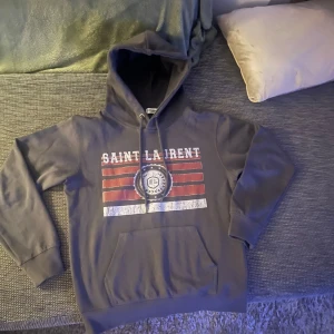 Grå hoodie från Saint Laurent - Säljer en hoodie från saint Laurent som inte säljs längre. Den passar någon mellan 165-175. Den är i nyskick och är riktigt snygg.