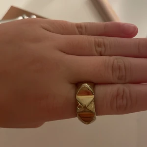 Guldfärgad ring från edblad - Snygg guldfärgad ring med ett unikt geometriskt mönster. Ringen har en bred design och en glansig yta som ger ett modernt och stilrent intryck. Perfekt för att ge en extra touch till din outfit. Från edblad