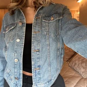 Blå jeansjacka från GinaTricot - Säljer en klassisk blå jeansjacka från Gina tricot i storlek M. Jackan har knappar framtill och två bröstfickor med knappstängning. Perfekt för en avslappnad stil.