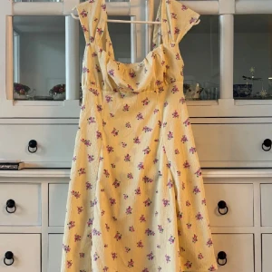 Blommig klänning från Gina Tricot - Blommig klänning från Gina Tricot i en ljus gul nyans med små rosa blommor. Klänningen har en söt omlott-detalj vid bysten och breda axelband. Perfekt för en somrig look!