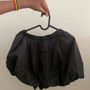 Svart ballongkjol - Säljer en svart ballongkjol med elastisk midja. Kjolen har en unik form som ger en voluminös och trendig look. Perfekt för att skapa en statement outfit.