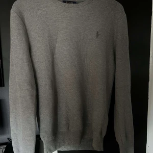 Grå tröja från Ralph Lauren - Säljer en stilren grå tröja från Ralph Lauren i bomull. Tröjan har en diskret broderad logga på bröstet och rund halsringning. Perfekt för en avslappnad och elegant look.