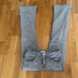 Grå jeans från Gina Tricot - Snygga low waist och bootcut grå jeans från Gina Tricot med slitna detaljer. De har en klassisk femficksdesign och stängs med två knappar och dragkedja. Perfekta för en avslappnad stil.