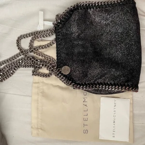 Svart glittrig axelväska från Stella McCartney - Säljer min favorit Stella McCartney mini fallabella väska, dustbag samt tags medföljer. På utsidan är den som ny, på insidan har ”påsen” lossnat lite men går säkert att sy ihop❤️ pris kan diskuteras vid snabb affär BYTER INTE