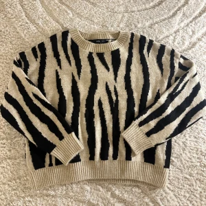 Zebramönstrad tröja från MANGO - Säljer en cool zebramönstrad tröja från MANGO i beige och svart. Tröjan har långa ärmar och ribbade muddar vid ärmslut och nederkant. Perfekt för att sticka ut i mängden!