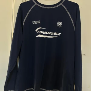 Mörkblå långärmad tröja med tryck - Säljer en mörkblå långärmad tröja med vitt tryck framtill. Tröjan har kontrastsömmar och rund halsringning. 