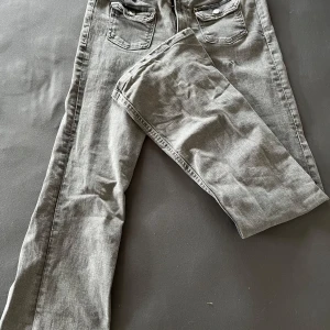 Grå jeans från Gina Tricot - Snygga grå jeans från Gina Tricot i en klassisk stil. De är bootcut och är perfekta för en avslappnad look. Jeansen har fickor både fram och bak samt knapp och dragkedja i gylfen. Fickorna där fram har väldigt fina knappar med silver färgad metal, jeansen har bara används ett fåtal gånger. 