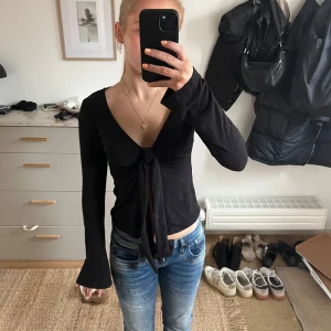 Svart långärmad topp med knyt - Snygg svart långärmad topp med knyt framtill. Perfekt för en stilren look. Toppen har en v-ringad design och är gjord i ett mjukt material. Använd fåtal gånger och har inga tecken på användning. Köpt för ca. 300 kr. Skriv privat för eventuella frågor💖