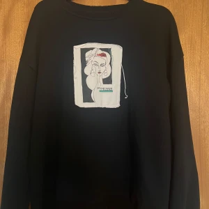 Svart sweatshirt med konstnärligt tryck - Säljer en svart sweatshirt med ett unikt konstnärligt tryck på framsidan. Trycket föreställer en stiliserad teckning av en kvinna med texten 'girls just wanna have fun'. Tröjan har en avslappnad passform och är perfekt för en casual look.