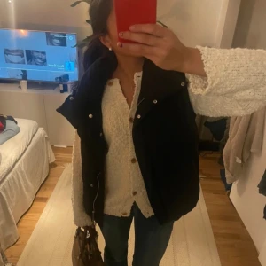 Svart väst från Bershka - Säljer en svart väst från Bershka. Västen har en hög krage och knappar framtill. Perfekt för lager-på-lager under kyligare dagar.