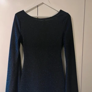Mörkblå glittrig klänning - Snygg mörkblå klänning med glittrigt material och öppen rygg. Köpt till nyår men kom hem för sent. Aldrig använd! Nypris 700kr. Peis kan diskuteras