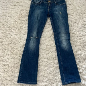 Blå jeans från Cross - Snygga blå jeans från Cross med slitna detaljer och en klassisk femficksdesign. De har en knappgylf och är tillverkade i ett robust denimtyg. Sitter jättefint på dock har de tyvärr blivit för små för mig! Storleken står ej men skulle säga W26