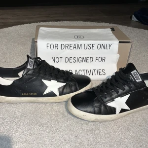 Svarta sneakers från Golden Goose - Snygga svarta sneakers från Golden Goose med vit stjärndetalj på sidan⭐️. Skorna har en klassisk design med snörning och en vit sula. Perfekta för en stilren look.😎 Säljer dessa för jag letar helt enkelt efter något nytt köpta här på plick har kvitto alltså från plick då. Killen jag köpte påstod att dem va äkta👌 och allt verkar tyda på de!! hör av er vid minsta fundering 💭 . Priset är inte hugget i sten.🪨 