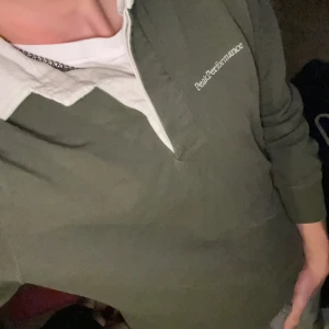 Olivgrön långärmad tröja från Peak Performance - Säljer en olivgrön långärmad tröja från Peak Performance med vit krage. Tröjan har en klassisk design med broderad logotyp på bröstet. Perfekt för en avslappnad stil. 