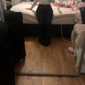 Bootcut Svarta skinn  jeans - Snygga svarta jeans med hög midja och tight passform lösare där nere vid benen. Perfekta för en stilren look. De har en klassisk design med knappar och dragkedja framtill.