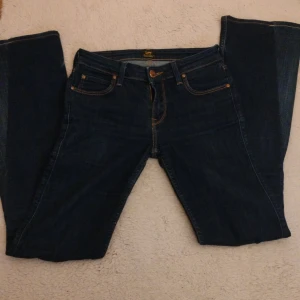 Lågmidjade bootcut jeans från Lee - Snygga mörkblå lågmidjade bootcut jeans från Lee med klassisk design. Har sytt ut benen till bootcut men inget som märks när de sitter på, de har en liten fläck på vänster knä som knappt märks! Står W27 i jeansen men hade sagt S/XS. Midjemått rakt över: 34cm, innerbenslängd: 80cm. Kontakta mig vid frågor!