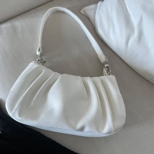 Vit axelväska - Snygg vit axelväska med ett stilrent och enkelt design. Väskan har en mjuk form och ett handtag som gör den lätt att bära. 