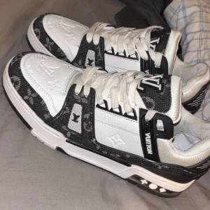 Svartvita sneakers - Snygga svartvita sneakers med ikoniskt monogrammönster. Skorna har en stilren design med snörning och en robust sula. Perfekta för den som vill ha en lyxig touch i vardagen.