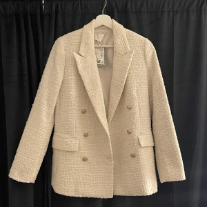 Vit kavaj med guldknappar - Elegant vit kavaj från H&M i ett strukturerat tyg med dubbelknäppning och stiliga guldknappar. Kavajen har en klassisk krage och långa ärmar, perfekt för en chic look 