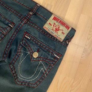 Jeans från True Religion - Snygga bootcut lågmidjade jeans från True Religion med unik och fin röd söm.  De har en unik broderad detalj på bakfickorna och knappar. (Bakfickorna är lite större än vanligt)  Dem är om sydda från en mer straight fit till mer bootcut. Dem är stl w32 men passar mig som har w29💓 Skriv till mig om frågor💞