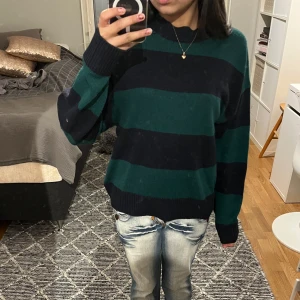 Randig tröja i grönt och svart - Säljer en mysig randig tröja i grönt och svart med långa ärmar. Perfekt för kyligare dagar. Tröjan har en avslappnad passform och är skön att bära.
