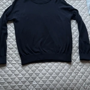 Marinblå merinoulltröja från Filippa K - Säljer en stilren marinblå tröja från Filippa K i 100% extra fin merinoull. Tröjan har en klassisk rund hals och långa ärmar, perfekt för kyligare dagar. Ett måste i garderoben för den som gillar tidlös design. 