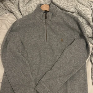 Grå tröja med dragkedja från Polo Ralph Lauren - Säljer en stilren grå tröja från Polo Ralph Lauren med halv dragkedja och broderad logotyp på bröstet. Perfekt för en avslappnad och snygg look. Size XL men går säkert bra för L