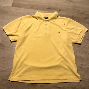 Gul kortärmad pikétröja från Ralph Lauren - Säljer en klassisk gul pikétröja från Ralph Lauren med korta ärmar och en broderad logotyp på bröstet. Perfekt för en avslappnad och stilren look.
