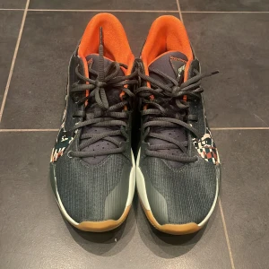 Basket skor Nike Air Zoom - Snygga Nike Air Zoom sneakers i svart och orange med unikt mönster på sidan. Skorna har snörning och en bekväm sula för optimal komfort. Perfekta för både träning, basket  och vardag.