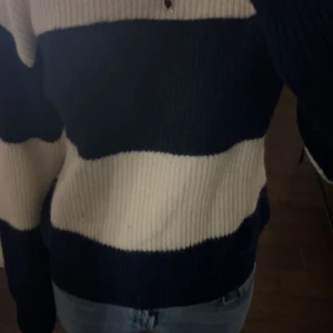 Randig stickad tröja i blått och beige - Mysig stickad tröja med breda ränder i mörkblått och beige. Tröjan har långa ärmar och en avslappnad passform, perfekt för kyligare dagar.